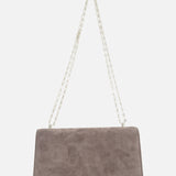 The Symmetry Chain Pouchette Bag by Savette is a rectangular taupe suede handbag featuring a long silver chain strap and an elegant turnlock closure, displayed against a white background.
