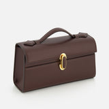 The Symmetry Pouchette Bag by Savette features a structured, rectangular silhouette in brown leather with a top handle and gold clasp, exuding quiet luxury on a white background. Meticulously crafted in Italy, this timeless and elegant piece showcases exceptional design and craftsmanship.