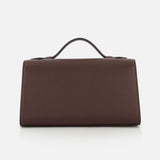 The Symmetry Pouchette Bag by Savette, a rectangular brown leather handbag with a top handle that embodies quiet luxury, is displayed against a plain white background.