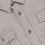 Close-up of the SEASE Glen Plaid Wool Overshirt, showcasing its light brown and beige glen plaid pattern with two chest pockets and plastic buttons. The collar and a portion of the label are visible at the top, emphasizing the refined wool texture inspired by the classic Prince of Wales check—making it an ideal option for business travel.