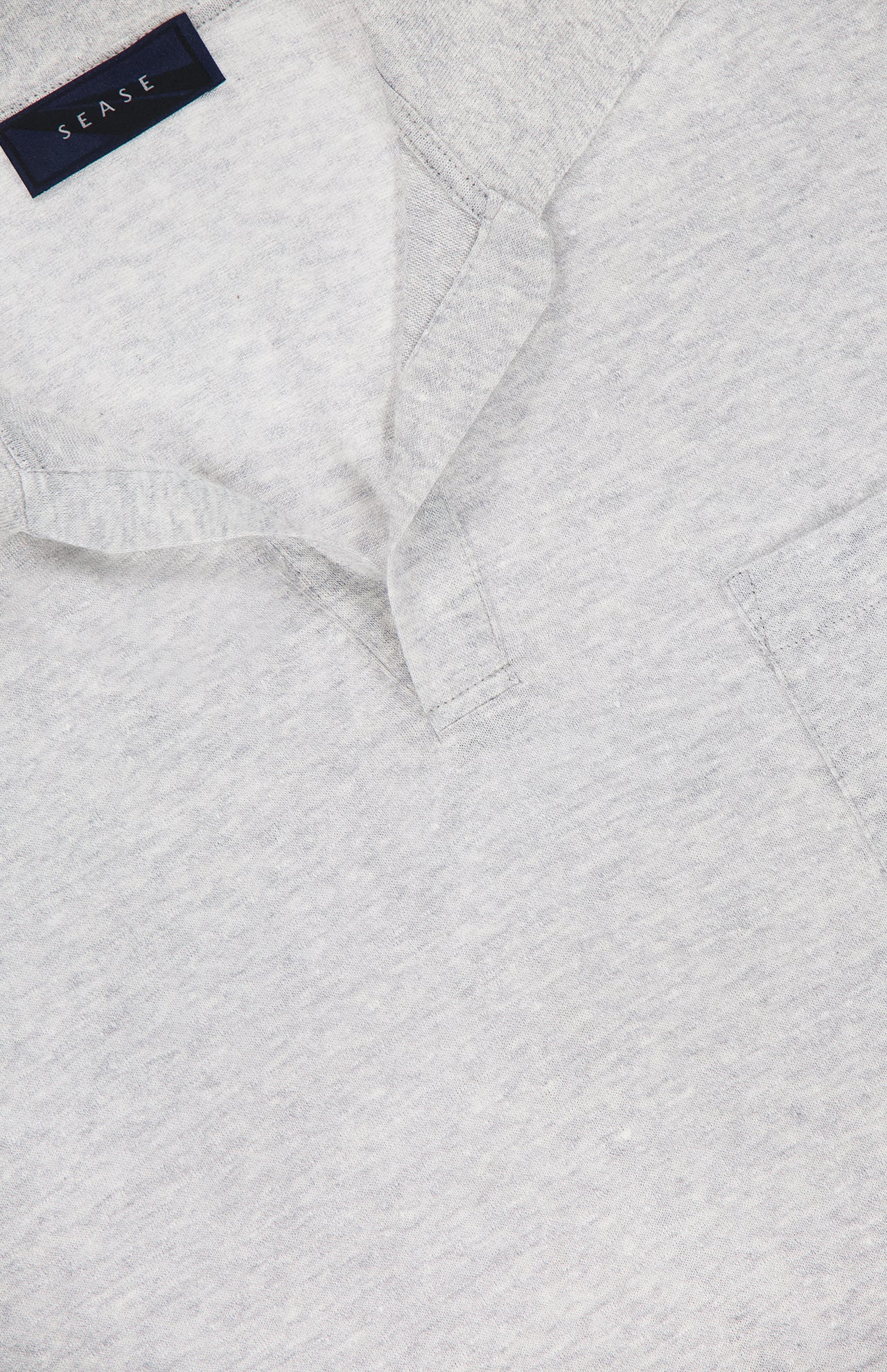 Close-up of the SEASE Linen Pocket Polo Shirt in light grey linen-blend fabric, with a subtle Johnny collar, short placket, small chest pocket, and a visible dark blue SEASE tag inside the neckline.
