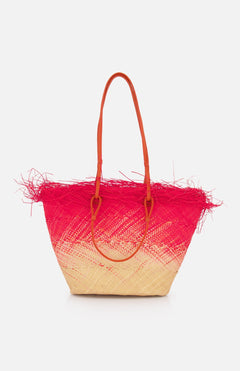 The SENSI STUDIO Medium Basket with Frayed Border Bag is a woven toquilla straw tote from Ecuador, featuring long brown handles, a beige-to-pink gradient design, and pink straw fringe along the top edge.