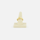 The SPINELLI KILCOLLIN Agon Vulcan Ring, featuring an elegant yellow gold knot design, is displayed on a beige cone stand against a plain white background.