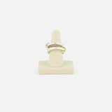 The SPINELLI KILCOLLIN Libra Gris Diamond Ring, featuring a twisted gold design with small clear stones, is displayed upright on a beige ring stand against a plain white background.