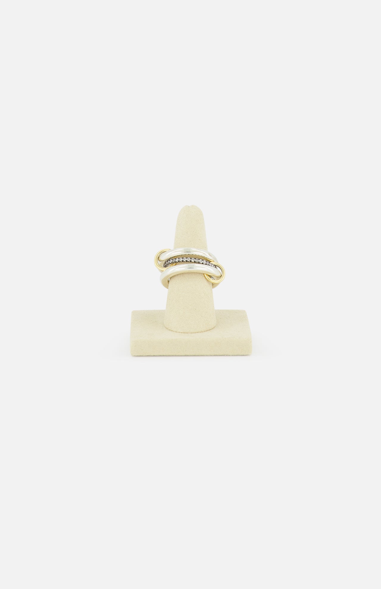 The SPINELLI KILCOLLIN Libra Gris Diamond Ring, featuring a twisted gold design with small clear stones, is displayed upright on a beige ring stand against a plain white background.