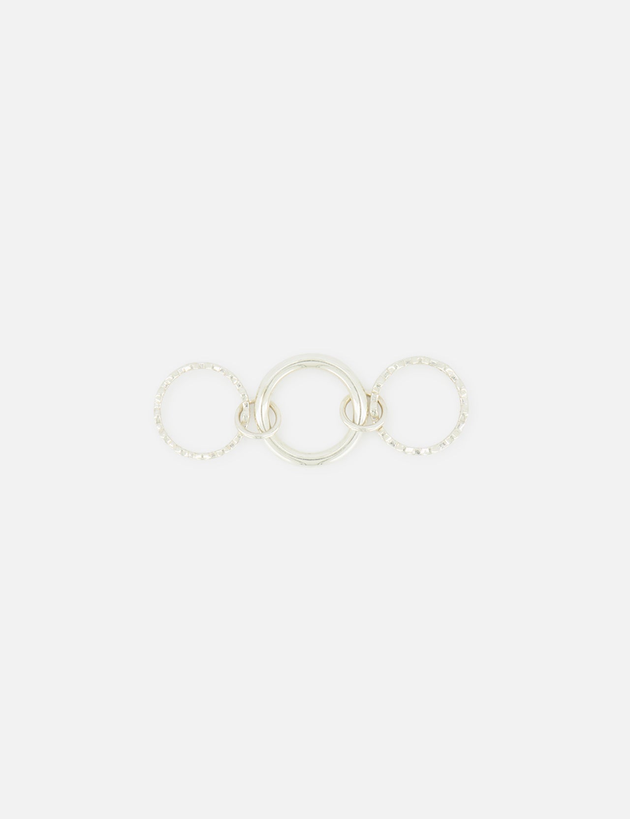The SPINELLI KILCOLLIN Microdame SK Ring features three interlocking sterling silver bands: a smooth, solid center ring flanked by two textured, beaded rings, all arranged horizontally on a plain white background.