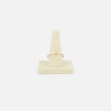 The SPINELLI KILCOLLIN Sirius 3 Annulets Ring, a delicate gold piece with a small rectangular gemstone, is displayed on a beige velvet ring stand against a plain white background.