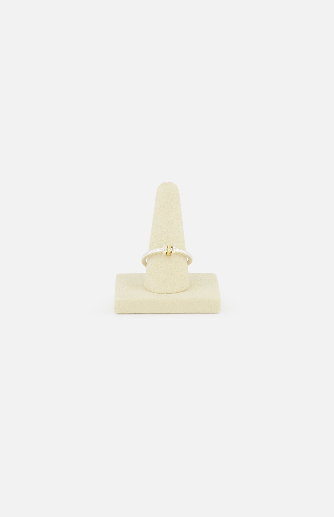The SPINELLI KILCOLLIN Sirius 3 Annulets Ring, a delicate gold piece with a small rectangular gemstone, is displayed on a beige velvet ring stand against a plain white background.