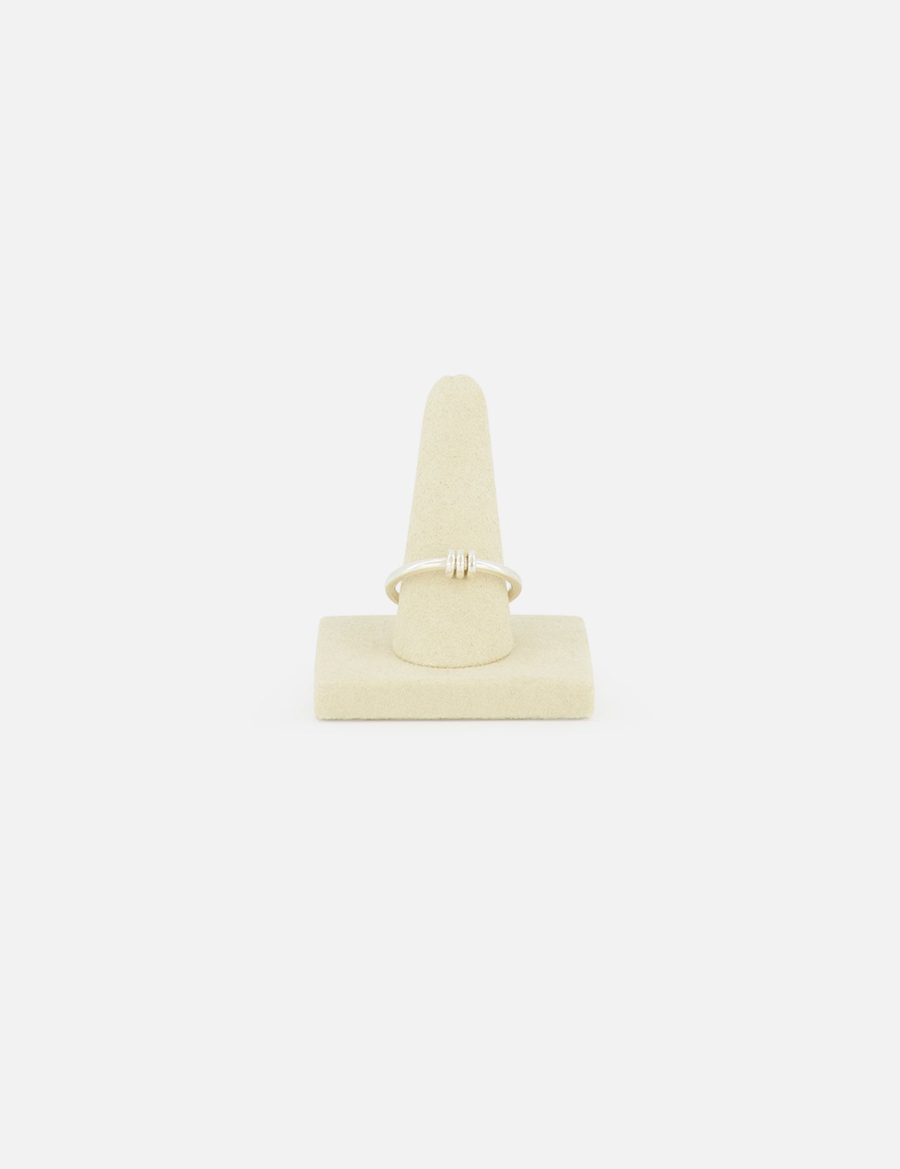 The Sirius 3 Annulets Ring by SPINELLI KILCOLLIN is a delicate, minimalist gold unisex ring with a small design, displayed on a beige suede stand against a plain white background.
