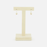 The Ara Deux Diamond Detail Earrings by SPINELLI KILCOLLIN, featuring gold annulets and dangling charms, are displayed on a beige T-shaped stand against a white background.