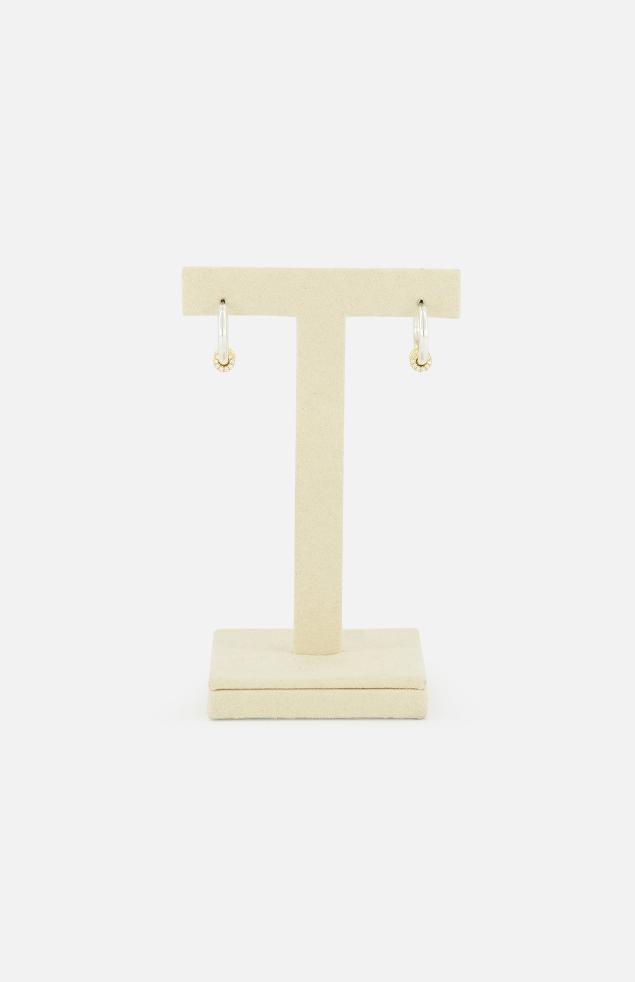 The Ara Deux Diamond Detail Earrings by SPINELLI KILCOLLIN, featuring gold annulets and dangling charms, are displayed on a beige T-shaped stand against a white background.