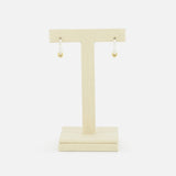 The SPINELLI KILCOLLIN Ara Deux Diamond Detail Earrings, a pair of small gold hoops, are displayed on a beige T-shaped jewelry stand against a plain white background.
