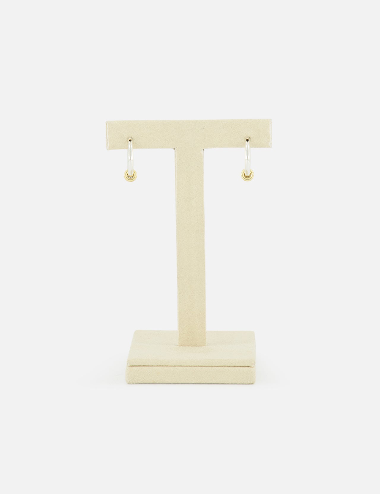 The SPINELLI KILCOLLIN Ara Deux Diamond Detail Earrings, a pair of small gold hoops, are displayed on a beige T-shaped jewelry stand against a plain white background.