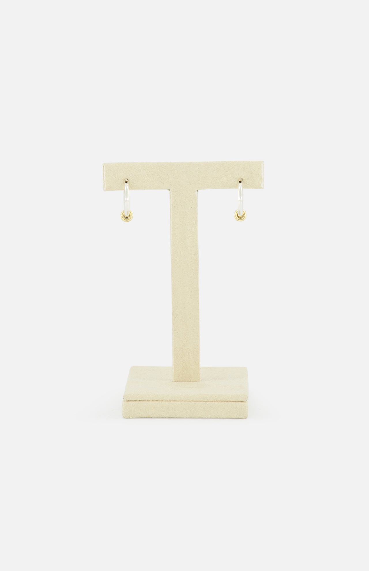The SPINELLI KILCOLLIN Ara Deux Diamond Detail Earrings, a pair of small gold hoops, are displayed on a beige T-shaped jewelry stand against a plain white background.