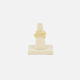 The SPINELLI KILCOLLIN Polaris 4 Band Ring, featuring a yellow gold knot design with small embedded stones, is displayed upright on a beige ring stand against a plain white background.