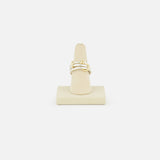 The SPINELLI KILCOLLIN Raneth 3 Band Ring, featuring a minimalist gold knot design, is shown upright on a beige ring stand against a plain white background.