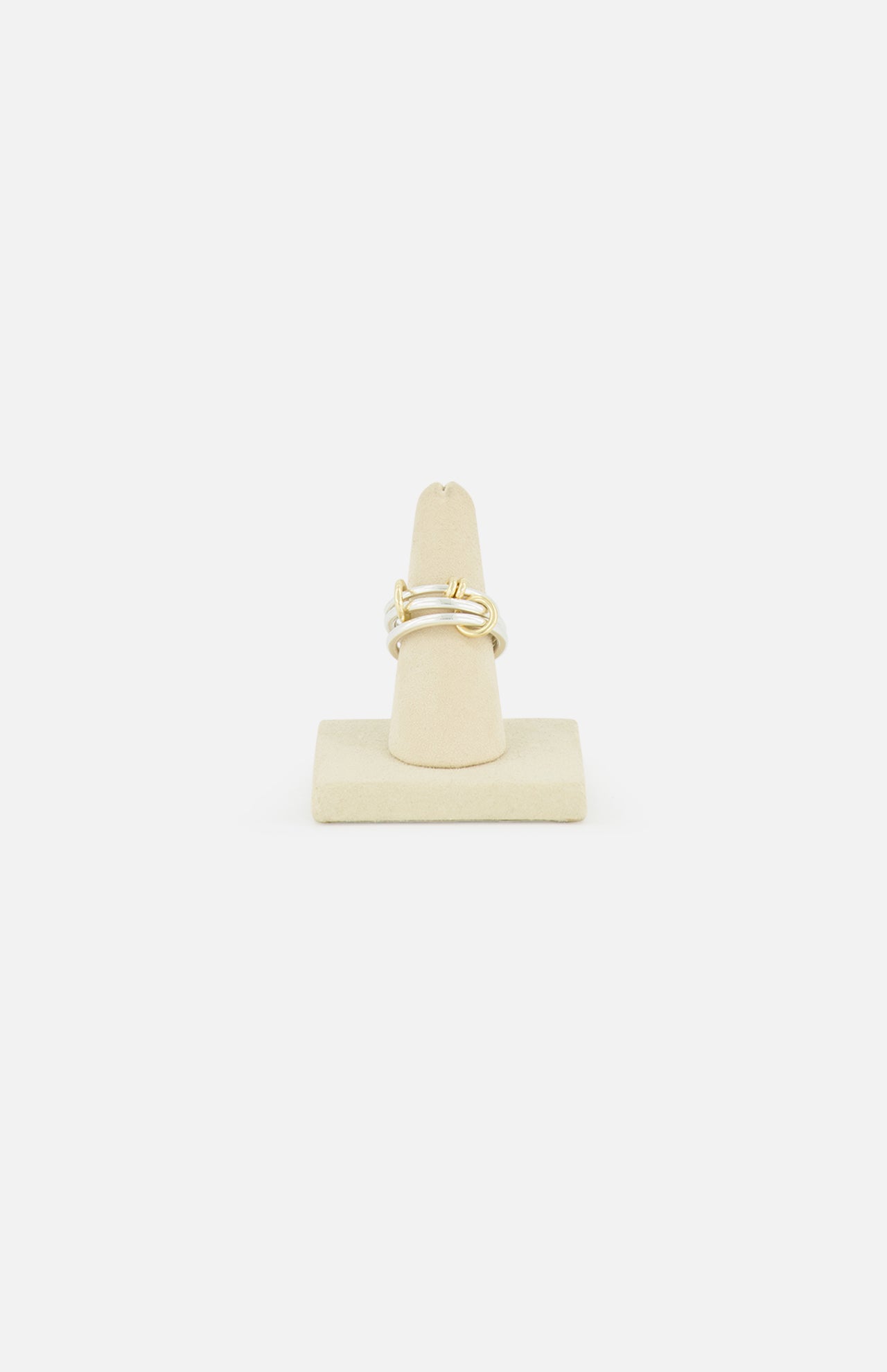 The SPINELLI KILCOLLIN Raneth 3 Band Ring, featuring a minimalist gold knot design, is shown upright on a beige ring stand against a plain white background.