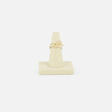 The SPINELLI KILCOLLIN Solarium 3 Band Ring showcases an abstract, intertwined design in sterling silver and yellow gold, presented on a beige ring stand against a plain white background.