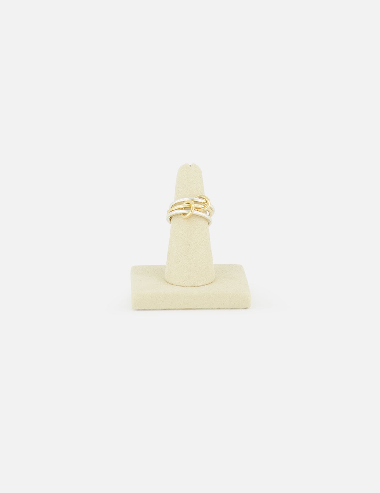 The SPINELLI KILCOLLIN Solarium 3 Band Ring showcases an abstract, intertwined design in sterling silver and yellow gold, presented on a beige ring stand against a plain white background.