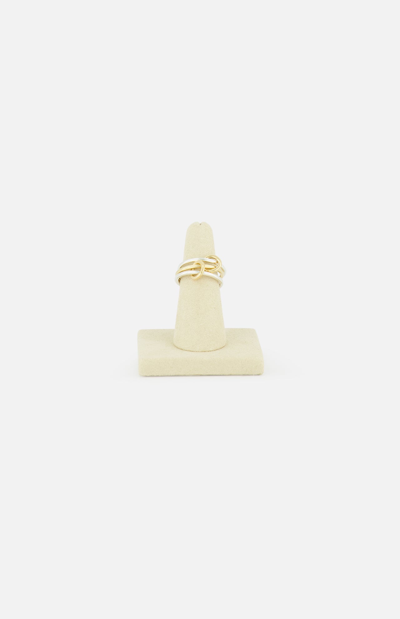 The SPINELLI KILCOLLIN Solarium 3 Band Ring showcases an abstract, intertwined design in sterling silver and yellow gold, presented on a beige ring stand against a plain white background.