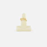 The SPINELLI KILCOLLIN Sonny Pavé Band Ring in yellow gold, featuring a twisted design with pavé diamonds, is displayed upright on a beige ring holder against a plain white background.