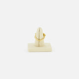 The SPINELLI KILCOLLIN Sonny Pavé Band Ring in yellow gold is displayed on a beige vertical ring holder, set against a plain white background to highlight the brand’s signature style.