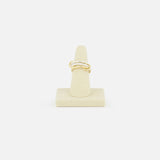 The SPINELLI KILCOLLIN Tigris Pavé Band Ring, featuring a twisted gold design with small pavé diamonds, is displayed upright on a beige stand against a white background, highlighting its modular elegance.