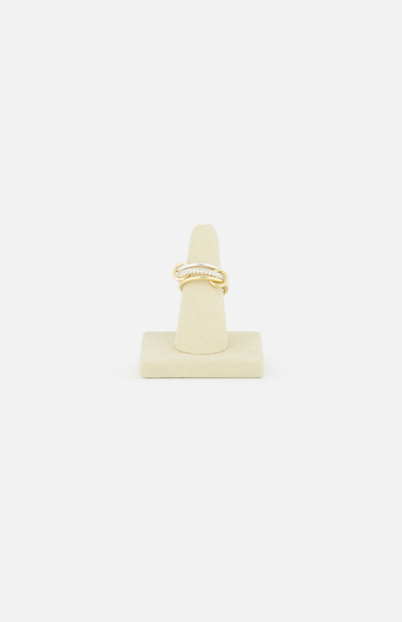 The SPINELLI KILCOLLIN Tigris Pavé Band Ring, featuring a twisted gold design with small pavé diamonds, is displayed upright on a beige stand against a white background, highlighting its modular elegance.