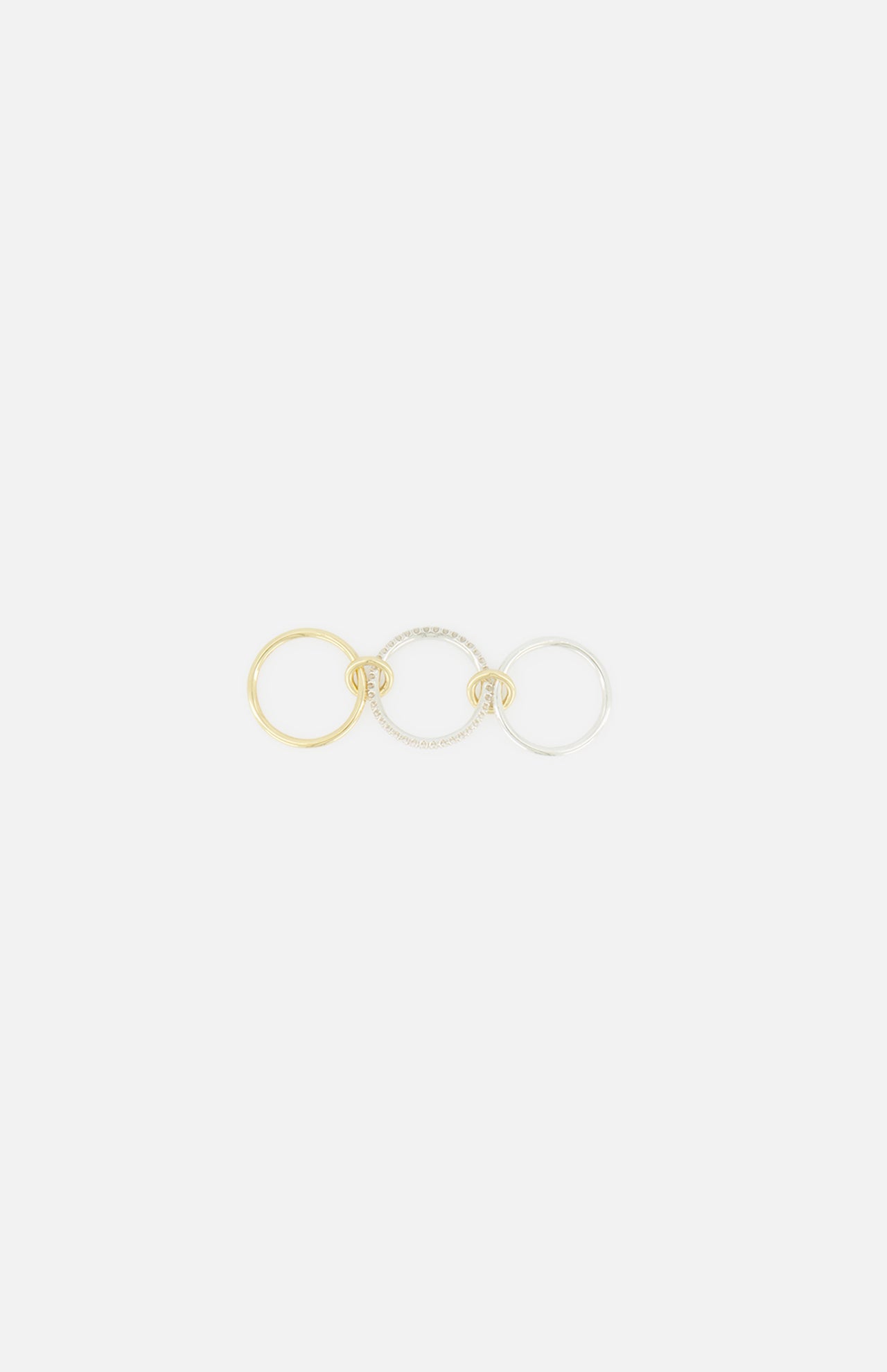 SPINELLI KILCOLLIN’s Tigris Pavé Band Ring is shown alongside gold and silver rings, each with a small knot detail, reflecting the brand’s modular jewelry style. The pavé ring is accented with clear stones.