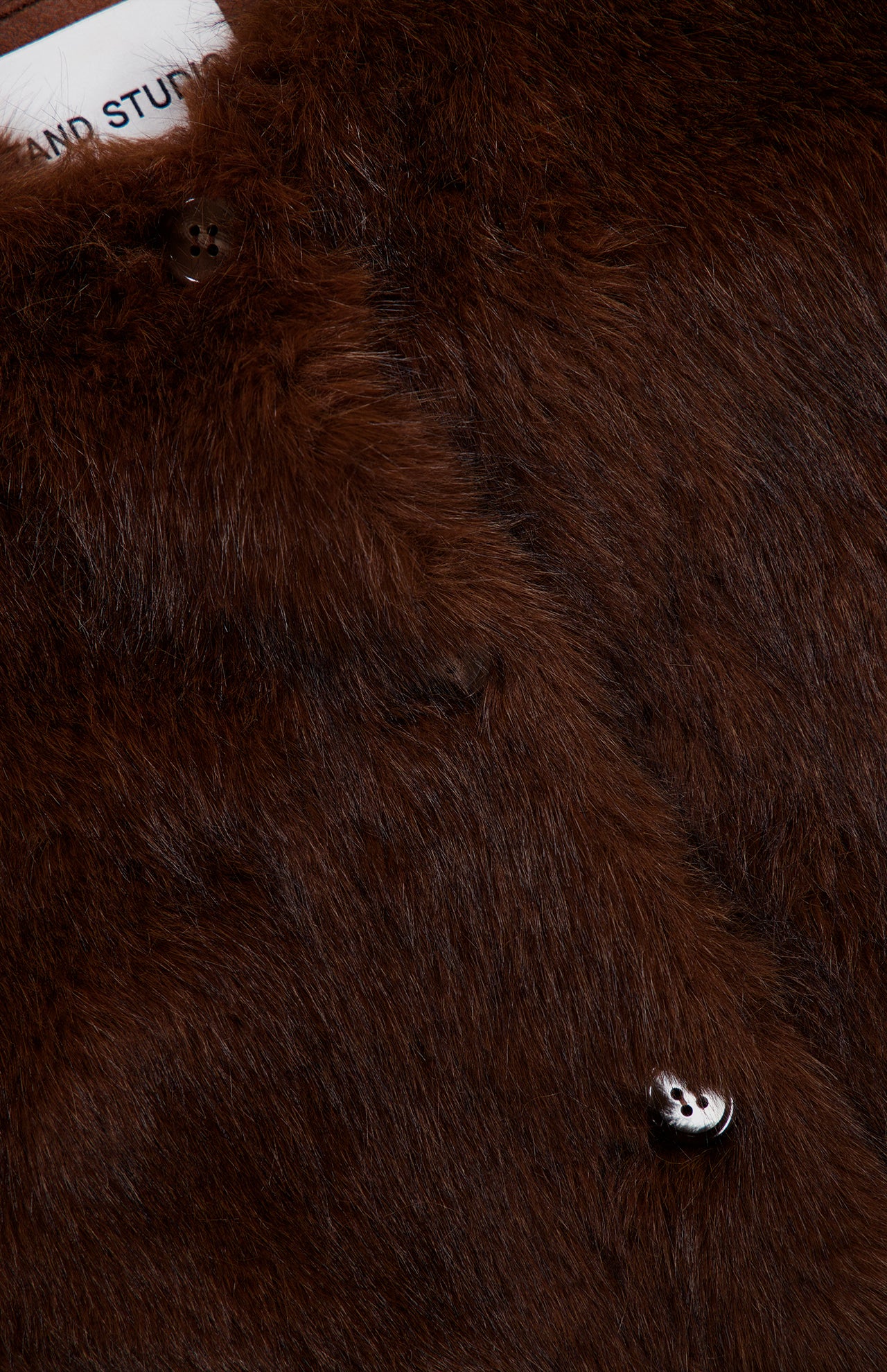 Close-up of a brown, long-haired Siena Collarless Jacket in luxury faux fur with a button placket.