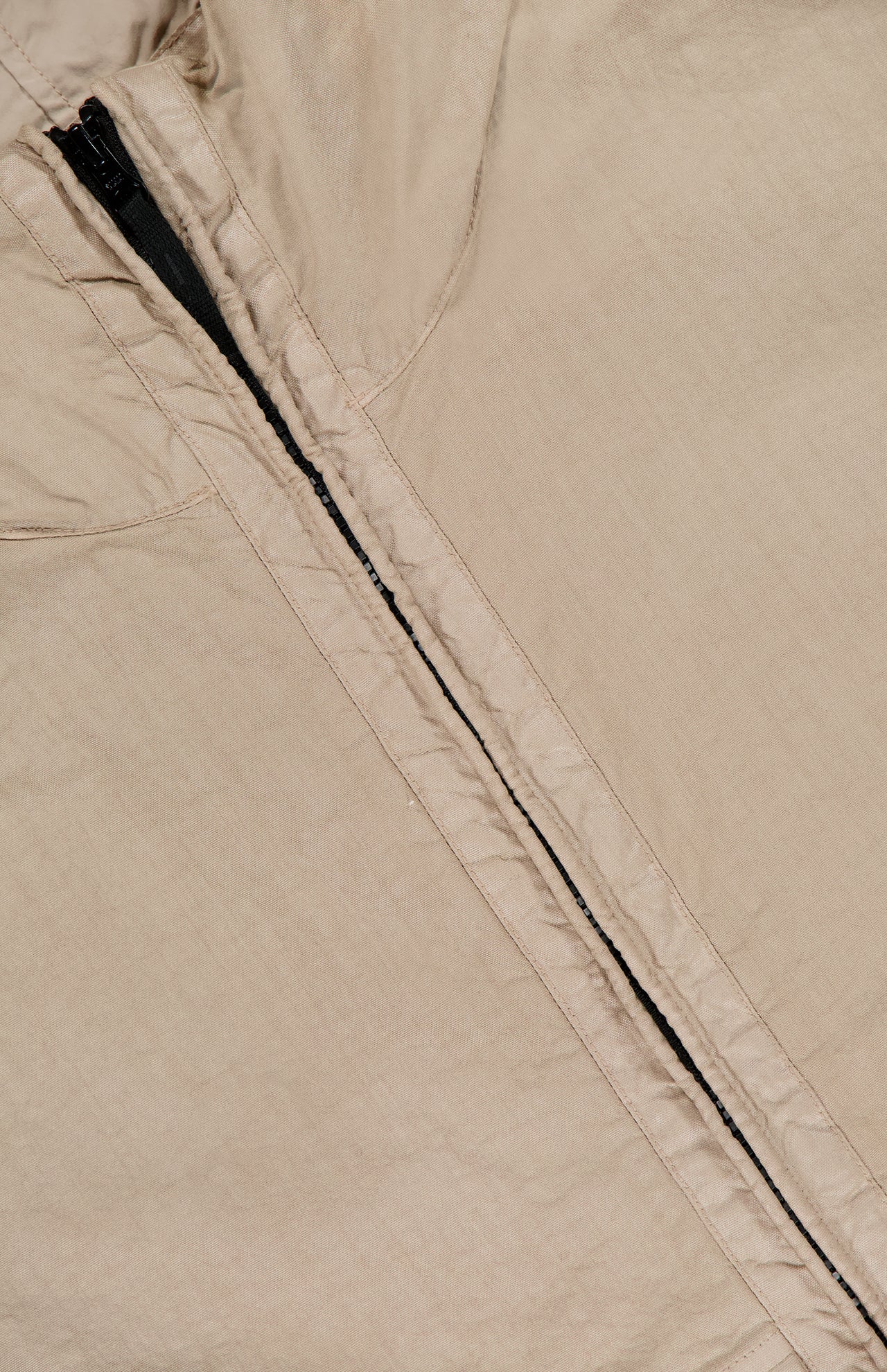 Close-up of the STONE ISLAND Hooded Full Zip Drawcord Jacket in beige, showcasing a vertical black zipper and detailed stitching inspired by innovative Japanese fabric—ideal for streetwear fans.