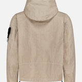 The STONE ISLAND Hooded Full Zip Drawcord Jacket in beige is shown from the back, crafted from innovative Japanese fabric with long sleeves, a signature arm patch on the left sleeve, elastic cuffs, and an adjustable drawstring hem.