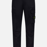STONE ISLAND Cotton Stretch Cargo Trouser Pants in black, featuring side pockets and a button closure. A yellow and green circular Stone Island logo patch accents one pocket. These streetwear-inspired cargo pants are showcased against a plain white background.