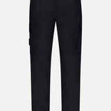 Back view of STONE ISLAND Cotton Stretch Cargo Trouser Pants in black, showcasing belt loops, flap-closure side pockets, and a single back pocket against a plain white background. These pants offer streetwear appeal with a straight-leg fit and prominent stitching details.