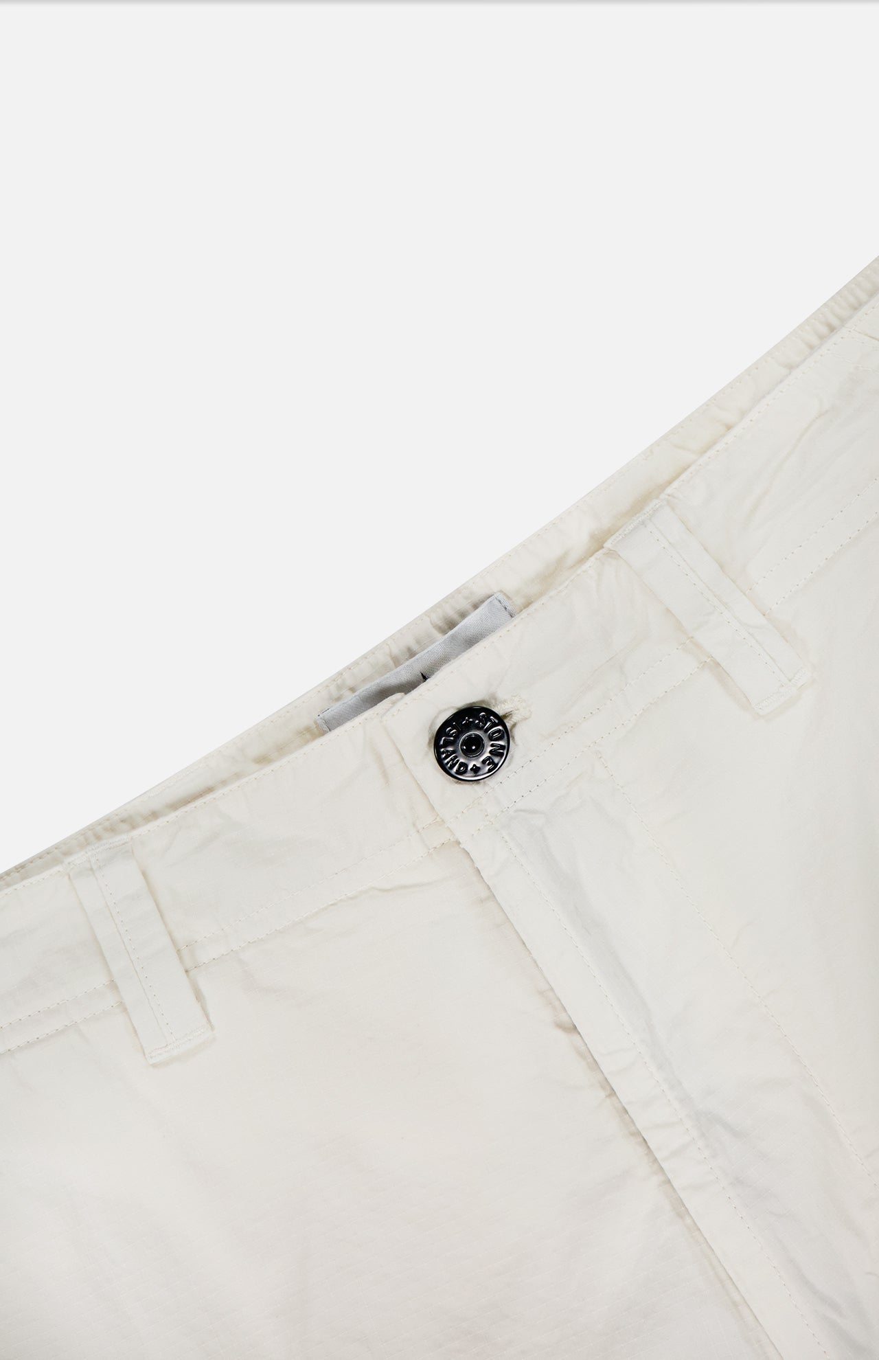 Close-up of the waistband and button fly of off-white STONE ISLAND Cargo Trousers, showcasing belt loops, a metal button, and visible stitching on a plain background.
