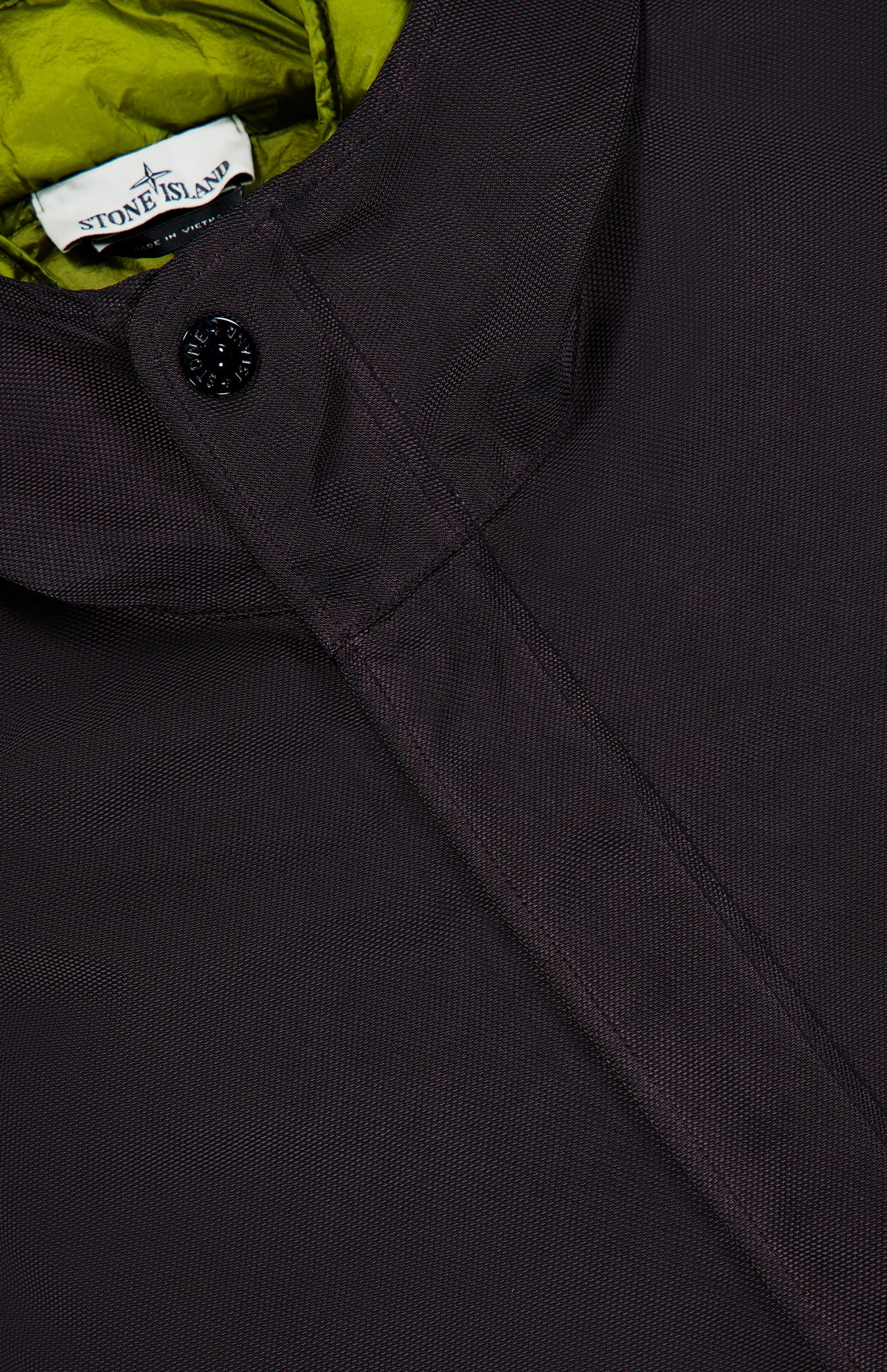 Close-up of a dark textured STONE ISLAND Double Layer Long Parka Coat with a black button, showing a yellow-green inner lining and the STONE ISLAND label near the collar.