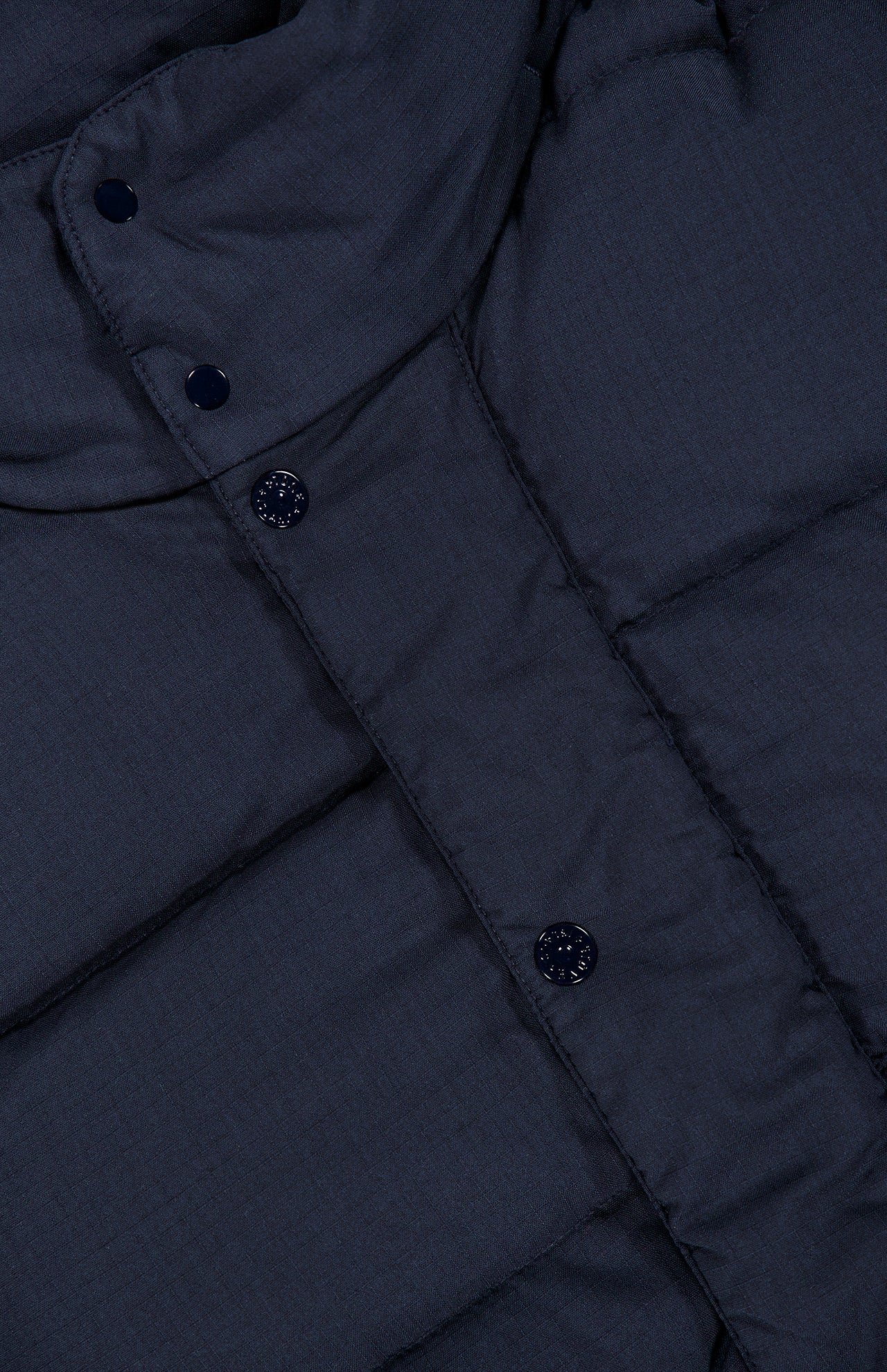 Close-up of a dark navy Stone Island Ghost Hooded Puffer Jacket featuring a detachable hood and a snap-button placket.