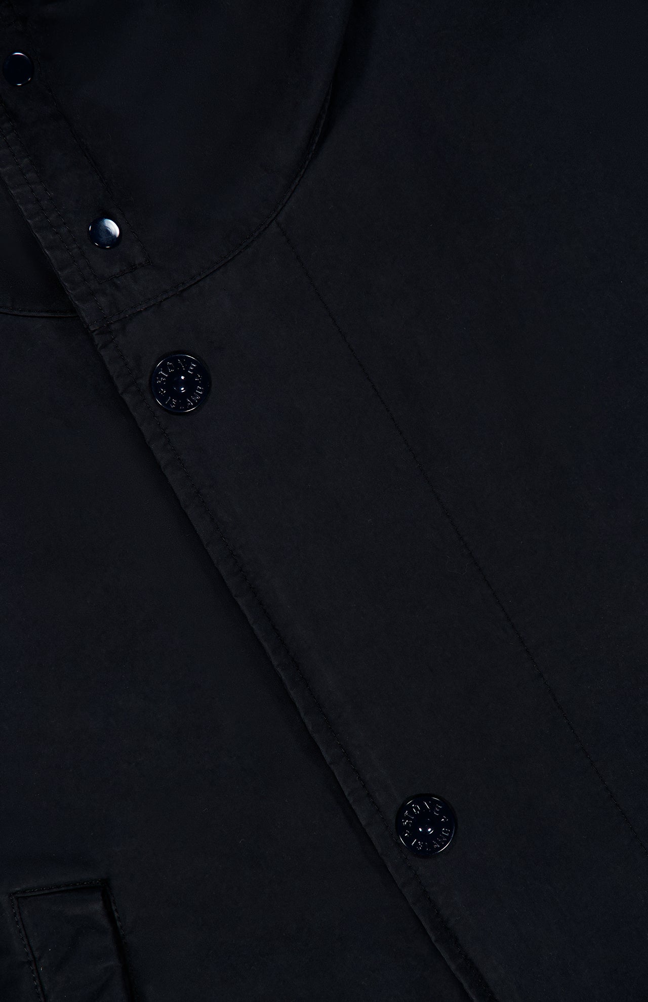 Close-up of the STONE ISLAND Ghost Hooded Short Parka Coat, showcasing its dark fabric, black buttons with subtle designs, and meticulous visible stitching—a refined men’s sportswear style characteristic of the brand. The smooth material and detailed buttons evoke signature elements often found in a Stone Island parka.