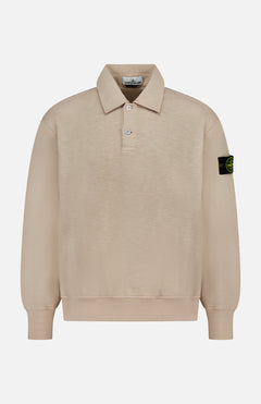 The Long Sleeve Polo Pullover Sweatshirt by STONE ISLAND features beige fabric, a collar with three buttons, and a black patch with yellow logo on the left sleeve, shown on a plain white background.