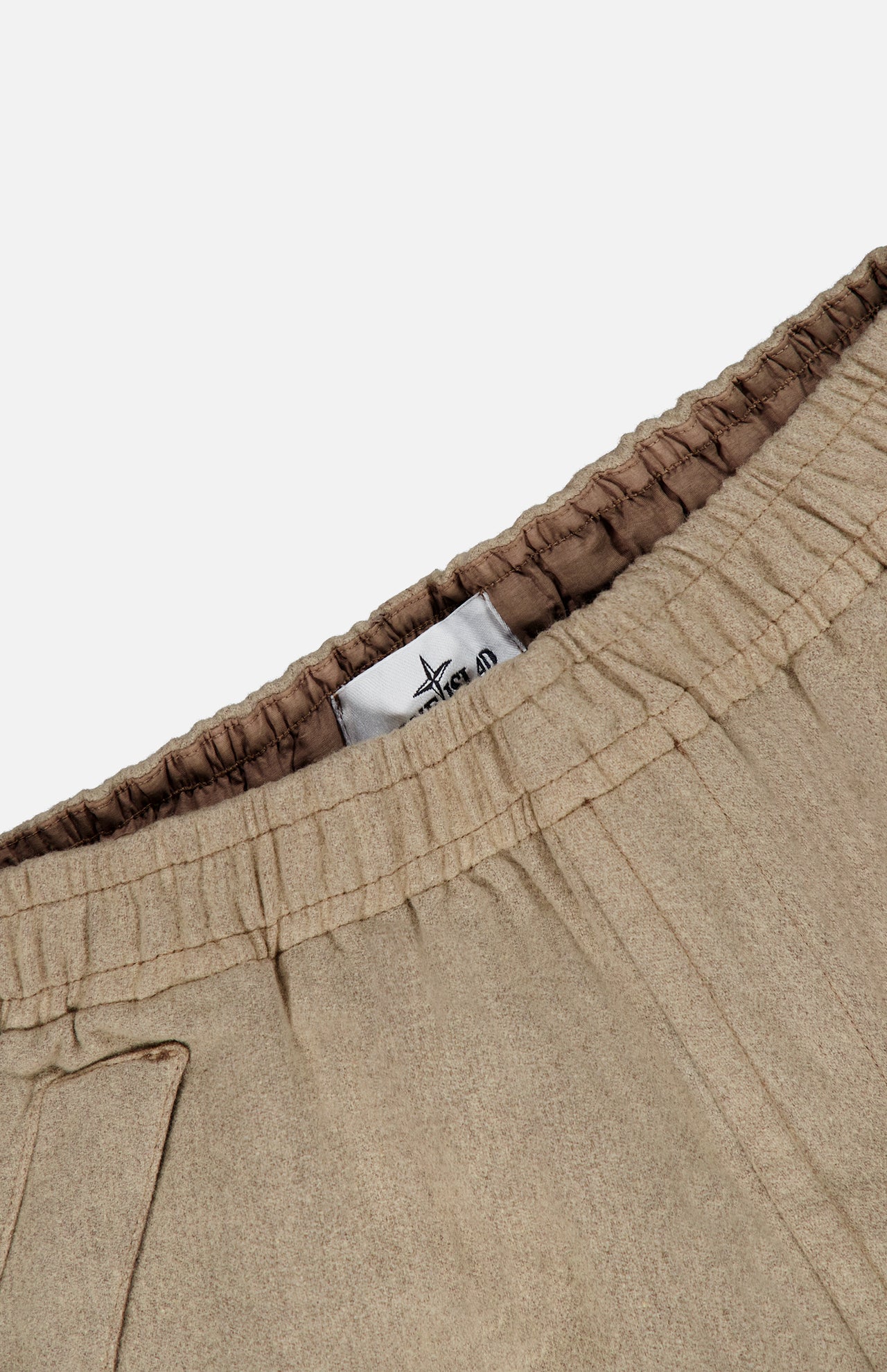 Close-up of the STONE ISLAND Loose-Fit Cargo Jogger Pant in beige, featuring an elastic waistband with visible stitching. A white tag with black text and the brand’s logo is sewn inside the waistband. The fabric has a soft, smooth texture reminiscent of premium wool sportswear.