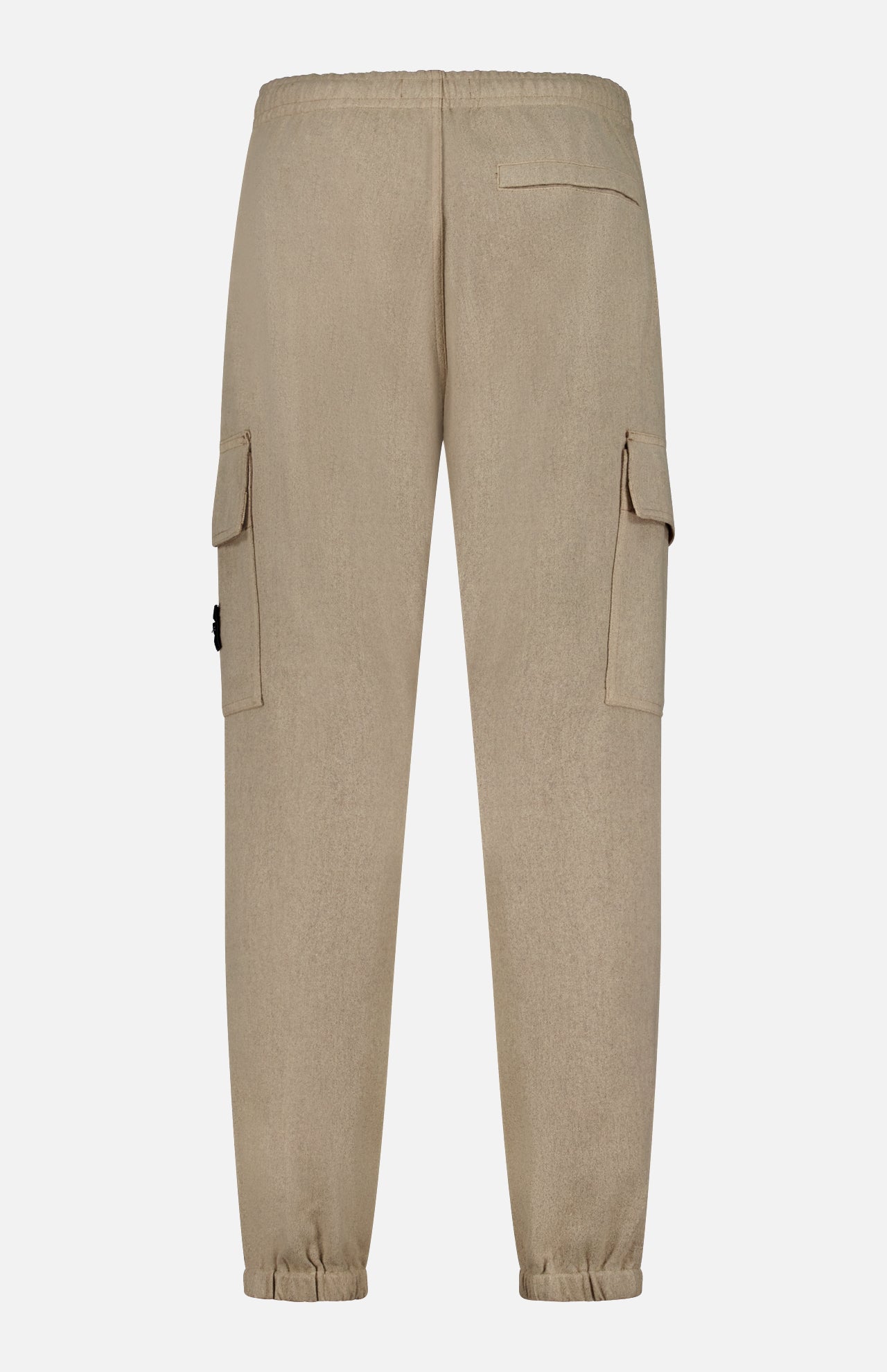 The STONE ISLAND Loose-Fit Cargo Jogger Pant features a beige colorway with an elastic waistband and cuffs, echoing the brand’s signature relaxed silhouette. Two side cargo pockets with flaps and a single back pocket add to its wool sportswear aesthetic. Displayed against a plain white background, the image highlights the back view of the pants.