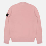 The Maglia Crewneck Sweater by STONE ISLAND is shown from the back in light pink, featuring ribbed cuffs and hem, plus a black logo patch on the left sleeve—blending modern street style with comfort.