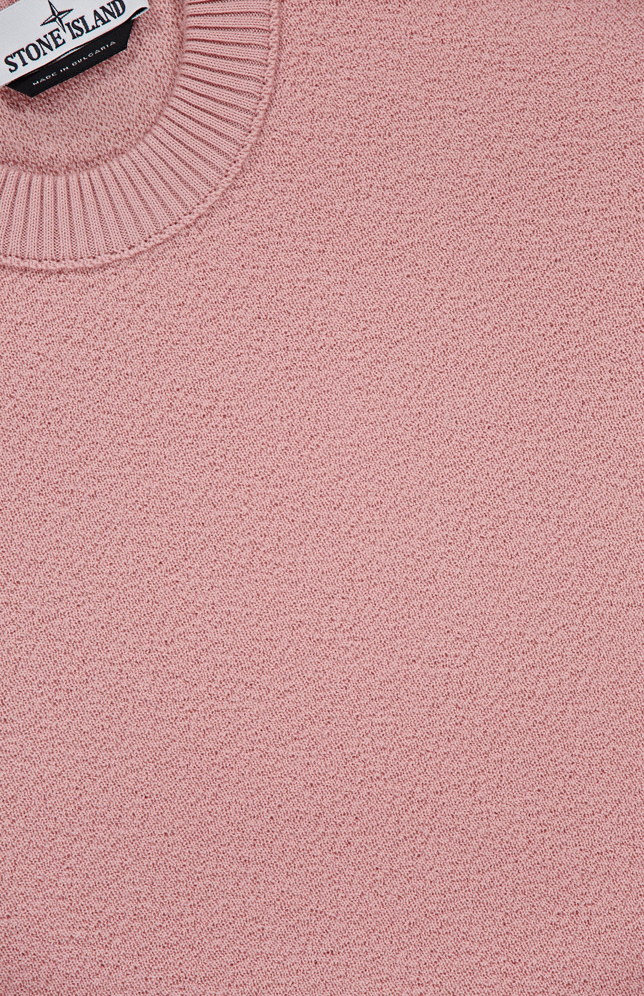 Close-up of the STONE ISLAND Maglia Crewneck Sweater in pink virgin wool, featuring a ribbed crewneck and part of the brand’s label—showcasing premium craftsmanship with modern streetwear style.