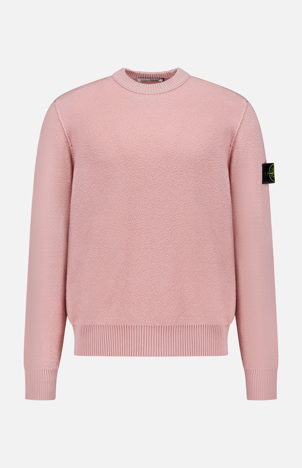 The STONE ISLAND Maglia Crewneck Sweater is a light pink, long-sleeve virgin wool top with ribbed cuffs and hem, and a black patch featuring the yellow-green circular logo on the left upper sleeve. Shown on a white background.