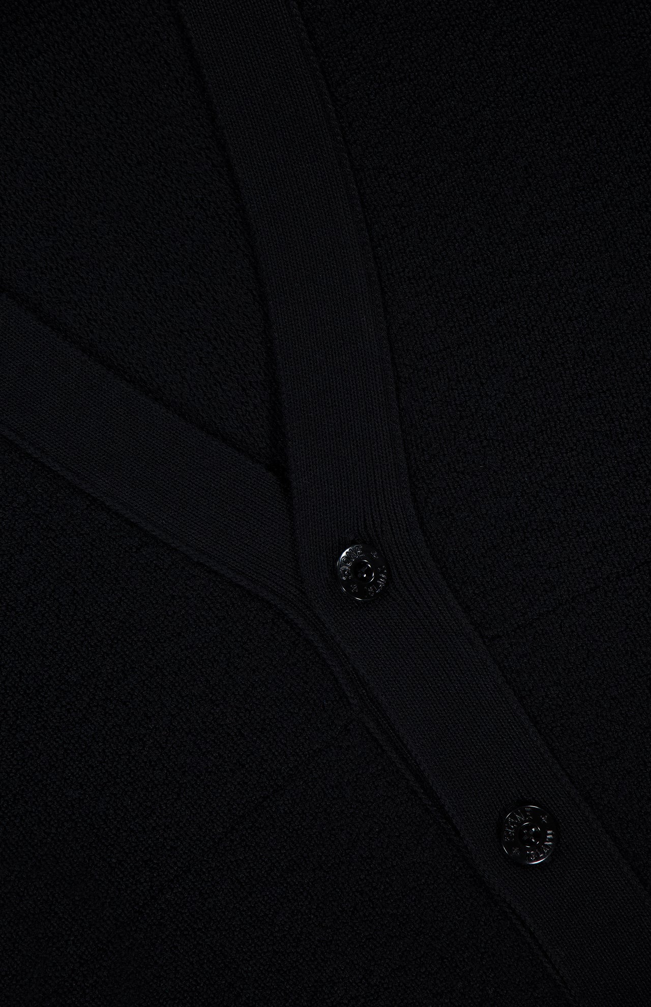 Close-up of a black textured fabric with two black buttons and a ribbed trim, likely part of the STONE ISLAND Maglia RWS Cardigan crafted from soft virgin wool.