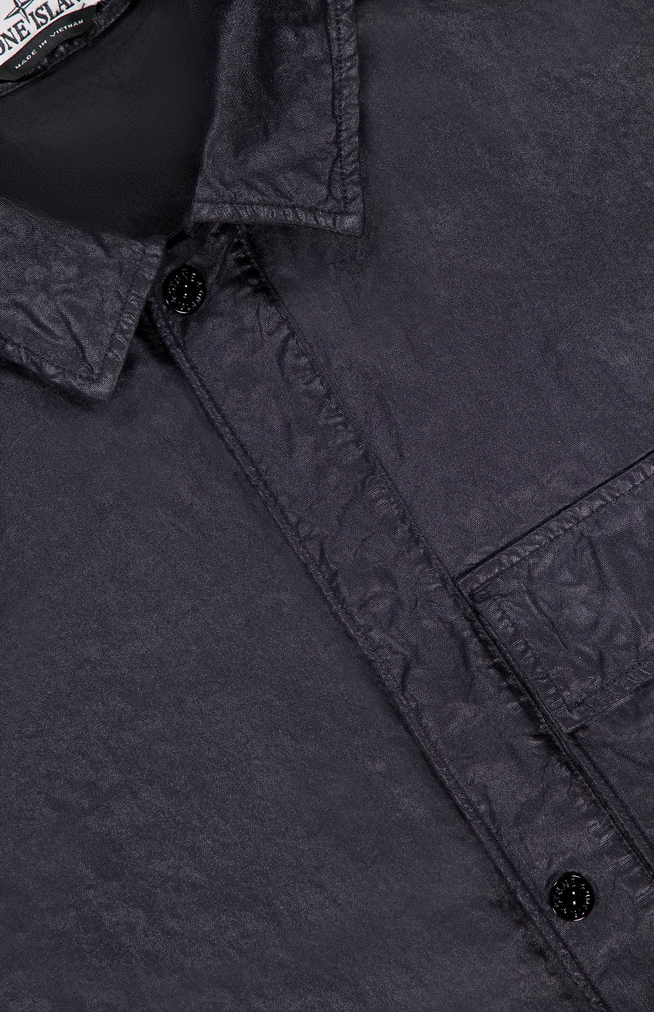 Close-up of the STONE ISLAND Crinkled Pocket Overshirt, featuring a visible collar, chest pocket, and two black buttons. The slightly shiny, crinkled fabric highlights the brand's signature technical sportswear look.