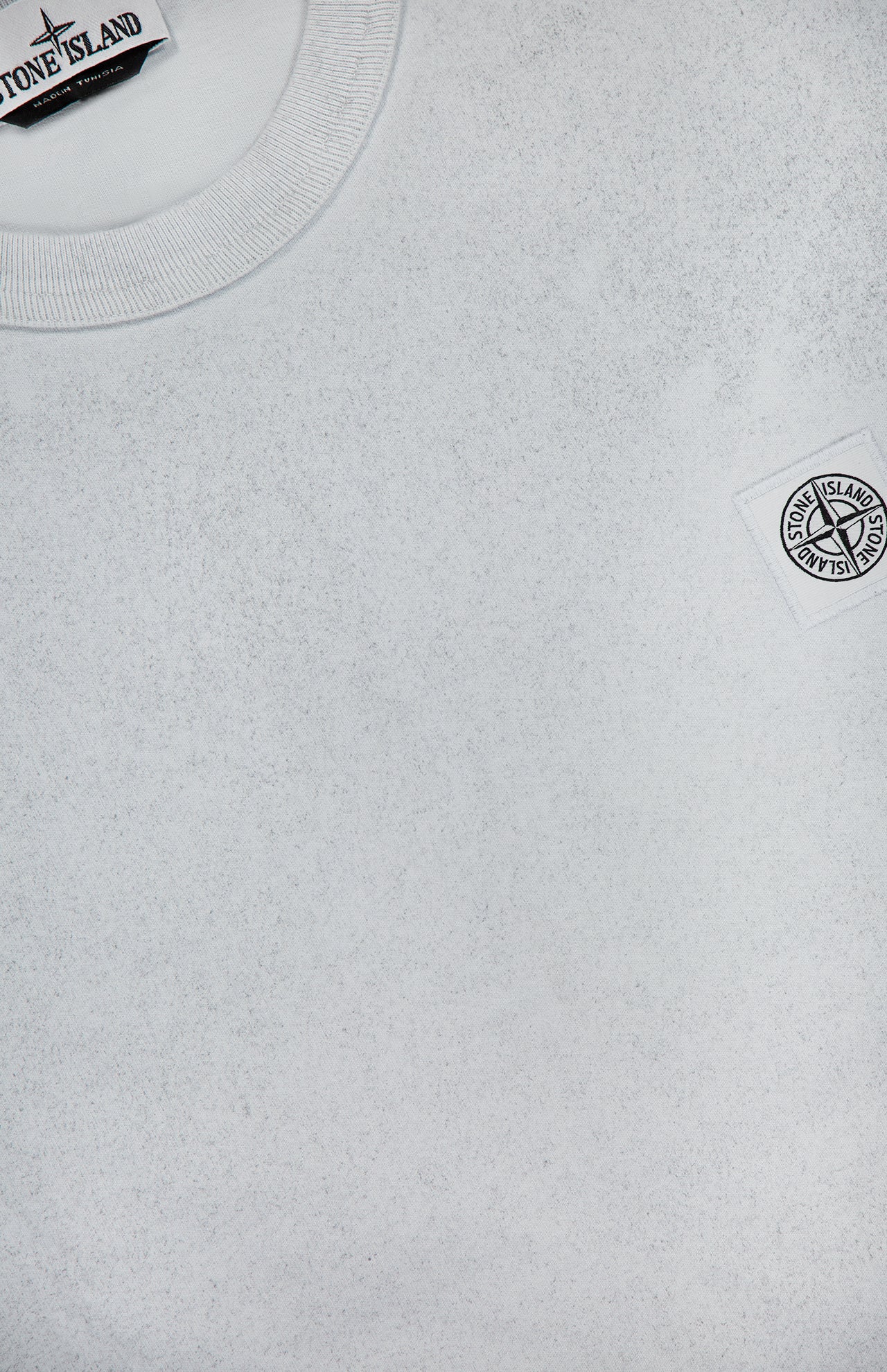 A close-up of the STONE ISLAND Reflected Short Sleeve T-Shirt, featuring a white color with detailed views of the collar and two signature logo patches—one at the neckline and one on the chest.