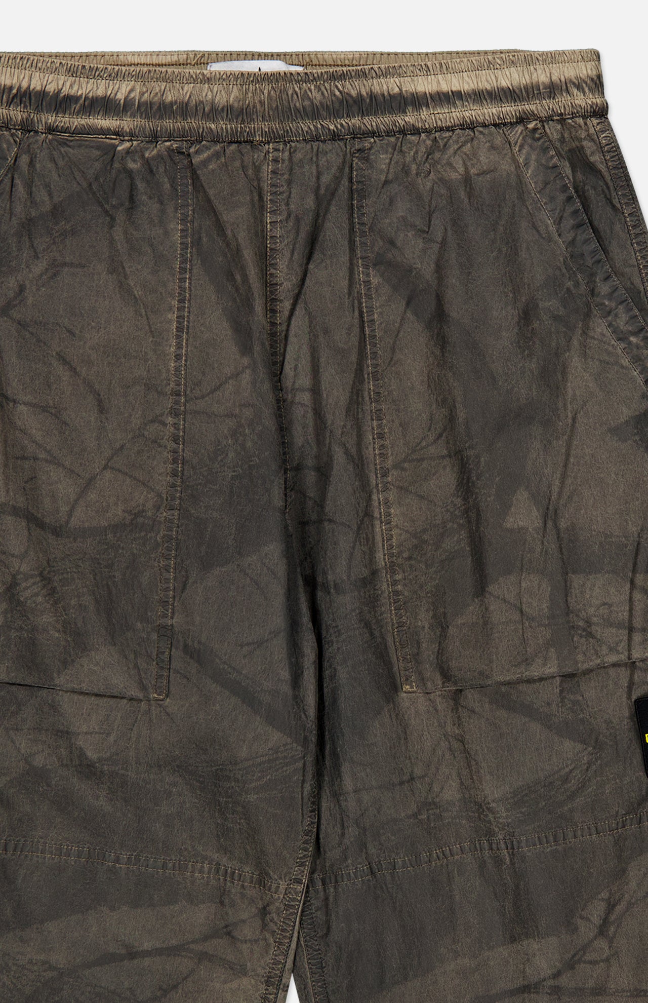 Close-up of the STONE ISLAND Regular-Fit Pattern Trousers in brown, showcasing crinkled fabric with side pockets, visible stitching, an elastic waistband, and a subtly textured finish—reflecting the brand’s signature technical construction.
