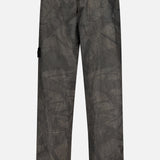 Back view of loose-fitting, dark gray STONE ISLAND Regular-Fit Pattern Trousers featuring a crinkled texture, elastic waistband, right-side flap pocket, and a small logo tag on the left leg that emphasizes their technical construction.