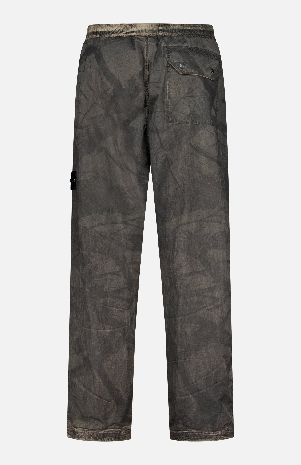 Back view of loose-fitting, dark gray STONE ISLAND Regular-Fit Pattern Trousers featuring a crinkled texture, elastic waistband, right-side flap pocket, and a small logo tag on the left leg that emphasizes their technical construction.